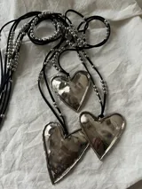 Collar con tres dijes de corazón irregular hechos a mano en alpaca o bronce, con tiento de gamuza negro y cuentas plateadas. El largo del tiento permite darle varias vueltas o usarlo largo.