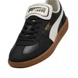 Championes Puma modelo Palermo, con diseño de perfil bajo en color negro con detalles en blanco y suela de goma color caramelo. Presentan el logo de la marca en dorado en el lateral y una lengüeta distintiva.