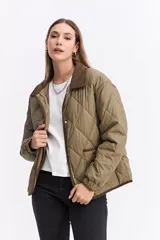 Campera matelaseada de diseño en rombos color verde oliva, con cuello y bordes en contraste color marrón. Presenta cierre frontal con botones a presión, mangas largas con puños elásticos y corte holgado.