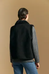 Chaleco negro de gamuza sintética con interior y bordes de corderito sintético. Presenta un diseño sin mangas con cuello solapa y cierre frontal.