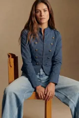 Chaqueta de estilo militar en color azul, confeccionada en algodón. Presenta cuello mao, cierre frontal con ganchos ocultos y doble hilera de botones decorativos metálicos. Incluye detalles de charreteras en los hombros.
