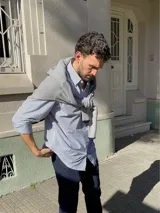 Camisa de corte clásico confeccionada en algodón, con diseño de rayas verticales finas en color rosa sobre fondo blanco. Presenta cuello abotonado, cierre frontal con botones, mangas largas con puños abotonados y un bolsillo en el pecho con el logo de la marca bordado.