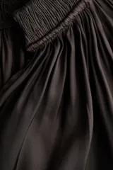 Blusa oversize corta color negro, confeccionada en tejido brillante. Presenta cuello nido de abeja con frunces y escote en V profundo, mangas globo largas de corte raglán y puños elásticos.