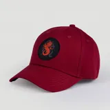 Gorro tipo baseball color bordó con visera curva y parche circular negro en el frente que presenta un dragón bordado en color naranja.
