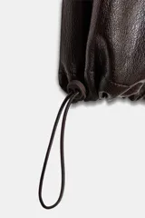 Pantalón de tiro alto confeccionado en material con efecto piel, con cintura elástica, bolsillos delanteros y nervio marcado en el frente. Presenta un diseño bombacho con bajo ajustable mediante cordones elásticos.