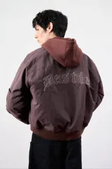 Campera bomber color marrón oscuro con cuello alto, puños y ruedo acanalados. Estampado en la espalda con la palabra "Bestia" en letras góticas.