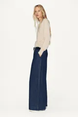 Jersey de punto color beige claro, manga larga y cuello redondo. Presenta un detalle de tejido a contraste (posiblemente una tela blanca con estampado sutil) asomando en el ruedo y el cuello.