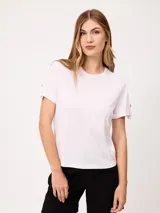Remera blanca de manga corta con vuelta en los puños y detalle de botón dorado. Presenta cuello redondo y corte recto.