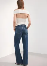 Jeans de tiro medio y corte wide leg, confeccionados en denim de algodón azul oscuro con lavado uniforme. Presentan cierre frontal con botón y cremallera, bolsillos laterales y traseros, y trabillas para cinturón.