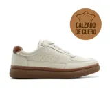 Championes casuales de cuero color crema, con detalles perforados en los laterales y suela de goma color marrón. Presenta un refuerzo en el talón en color marrón contrastante.