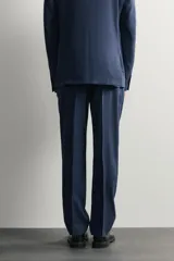 Pantalón de traje de corte regular fit en color azul marino, confeccionado en una mezcla de lino y lana. Cuenta con bolsillos delanteros, bolsillos traseros de doble vivo con botón y raya marcada en el centro de las piernas.
