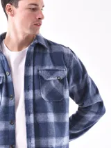 Sobrecamisa a cuadros azul y gris con cuello clásico, cierre frontal con botones, dos bolsillos con solapa abotonada en el pecho y puños abotonados.