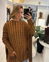 Sweater de tejido de punto con diseño de ochos, color beige, de corte holgado y manga larga con puños ajustados. Presenta dos bolsillos frontales tipo parche con detalle de etiqueta de cuero.