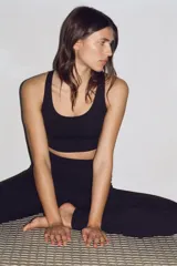 Top deportivo negro de sujeción media, con escote redondo y tirantes finos cruzados en la espalda. Presenta copas forradas con relleno extraíble y elástico cepillado en el bajo.