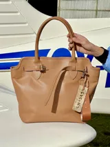 Bolso tipo tote de cuero color marrón claro, con doble asa de mano y correa fina ajustable. Incluye etiqueta colgante con inscripción.