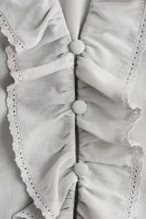 Blusa color gris claro en tejido de mezcla de viscosa y algodón, con escote en V pronunciado, volados frontales, alforzas, inserciones de encaje y detalles bordados. Cuenta con mangas abullonadas al codo con puños elásticos de volado y volado ancho en el bajo.