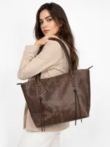 Cartera tipo tote bag de cuero vacuno marrón, con detalles de trenzado artesanal en los laterales y flecos colgantes decorativos. Cuenta con doble asa de hombro y cierre superior.