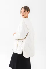 Chaqueta acolchada de color negro con diseño de costuras onduladas. Presenta cuello redondo, cierre frontal con botones a presión y dos bolsillos frontales tipo cargo con solapa y detalle de hebilla. Posee un corte holgado y mangas largas.
