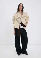 Chaqueta crop estilo gabardina corta color beige, de diseño recto, cuello alto tipo embudo, manga larga, bolsillos laterales y cierre cruzado de doble botonadura con botones oscuros. Con forro interior de poliéster.