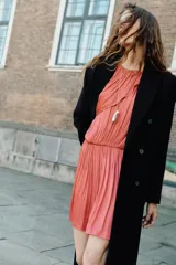 Vestido corto de cuello redondo con diseño de capa superpuesta y mangas asimétricas. Presenta cintura elástica y cierre posterior con botón.