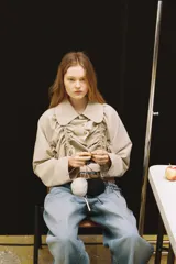 Chaqueta corta color beige, confeccionada en gabardina, con cuello solapa redondeado, mangas largas con frunces y detalle de frunces con lazada en el delantero, cerrando con botones.