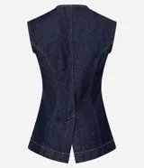 Chaleco largo de jean azul oscuro, con corte acinturado, cierre frontal abotonado y costuras con pespuntes en contraste. Presenta un diseño sin mangas con cuello redondo.