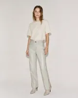 Pantalón flare de cuero vacuno en color hueso, con tiro alto y diseño ajustado con abertura en los tobillos.