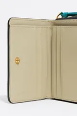 Billetera compacta de estructura rígida en piel vacuna color negro, con cierre de cremallera perimetral y tirador de tejido en color turquesa. Presenta el logo de la marca estampado en dorado en el frente.