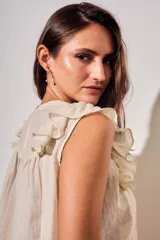 Blusa sin mangas de color crudo, con diseño oversize, cuello redondo y detalles de nido de abeja bordado en el pecho, acompañado de volados en los hombros.