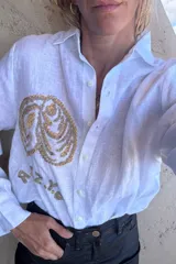 Camisa de lino color tostado, de manga larga y corte oversize, con bordado artesanal en hilo blanco en el frente y botones frontales.