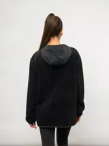 Buzo de polar negro con capucha, cierre frontal parcial y bolsillos laterales. Presenta detalles en nylon a tono en la capucha, la solapa del cierre y los bordes de los bolsillos, con el logo de la marca bordado en el pecho.