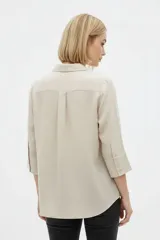 Camisa de algodón color beige, de corte holgado, con mangas tres cuartos, cuello camisero y cierre frontal de botones.