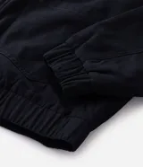 Campera de sarga de algodón con capucha, cierre frontal con cremallera y trabas metálicas decorativas. Presenta un bolsillo con cierre en la manga y puños elásticos, con un diseño de estilo utilitario.