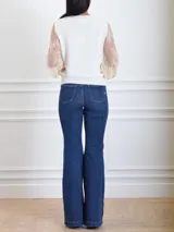 Pantalón denim azul con corte flare, ajustado en el muslo y con botones metálicos dorados en el lateral exterior.