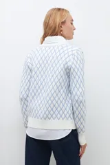 Cardigan de punto con diseño de rombos en color celeste sobre fondo blanco, cuello redondo y cierre frontal con botones.
