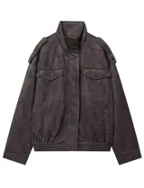 Chaqueta de gamuza en color marrón oscuro, con cuello alto, cierre frontal oculto y bolsillos tipo cargo en el pecho. Presenta un diseño de corte holgado con detalles de charreteras en los hombros.