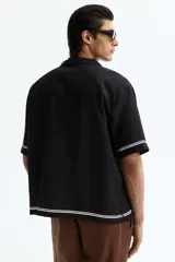 Camisa de manga corta de H&M, con corte relajado, cuello abierto estilo resort, tapeta frontal con botones y bajo recto. Diseño estampado en color blanco sobre base negra con motivos de palmeras, soles y estrellas.