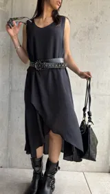 Vestido midi negro sin mangas, con escote redondo y corte asimétrico con volados. Incluye cinturón de cuero con tachas.