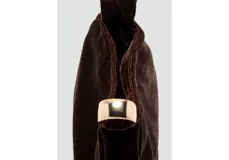 Bolso de mano pequeño confeccionado en terciopelo color marrón oscuro, con diseño fruncido y detalle de aro metálico dorado en el asa.