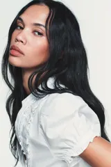 Camisa de popelín con cuello redondo y escote en pico, manga corta abullonada con elástico y cierre frontal con botones. Presenta detalles de volantes a lo largo de la abertura frontal.