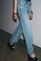 Jeans de tiro alto y corte ancho (wide leg) hasta el tobillo, confeccionados en denim azul de efecto lavado. Presenta cinco bolsillos y cierre frontal con cremallera y botón.