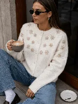 Cardigan de punto color blanco marfil, con cuello redondo, manga larga y cierre frontal de botones forrados. Presenta delicadas flores bordadas en relieve a lo largo del frente y las mangas.