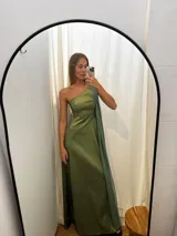 Vestido largo de fiesta color verde, confeccionado en tafeta con brillo y gasa. Presenta un diseño de un solo hombro con una capa de seda liviana integrada que permite diversas formas de uso, aportando movimiento y elegancia.