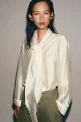 Camisa de tejido satinado con mezcla de lyocell, cuello redondo con escote en pico y lazada frontal. Presenta mangas largas con puños anchos y bajo recto.