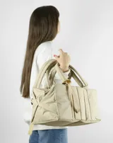 Bolso tipo tote color beige con diseño acolchado y doble asa de hombro.