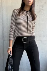 Remera de manga larga con diseño a rayas horizontales en color beige y negro, confeccionada en tejido de punto acanalado. Presenta un cuello redondo con un detalle de cordón fino negro que cae hacia el pecho.