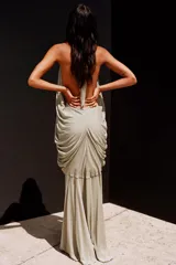 Vestido largo de viscosa en color beige, con diseño de cuello halter y escote en pico pronunciado. Presenta un cuerpo drapeado con volumen y espalda descubierta, con falda fluida y forro interior.
