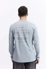 Remera de manga larga color celeste, con escote redondo y estampado frontal con la frase "FAVOR RAINS DOWN + ON ME" y el logo de Mistral.