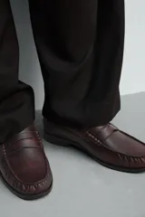Mocasín de vestir tipo penny loafer en color bordó con acabado desgastado, diseño de antifaz en el empeine y suela de goma a contraste con pequeño tacón.