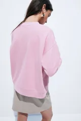 Buzo de corte relajado con cuello redondo y hombros caídos, confeccionado en tejido suave con interior cepillado. Presenta un diseño bordado en el pecho y ribetes acanalados en cuello, puños y bajo.